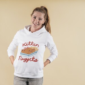 May include: White hoodie with a red and blue graphic of kittens in a box with the text "Kitten Nuggets".
