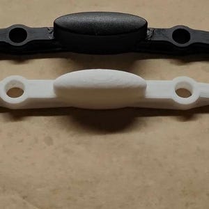 May include: Two plastic pieces, one black and one white, with a rounded top and two curved arms. The pieces are similar in shape and size.