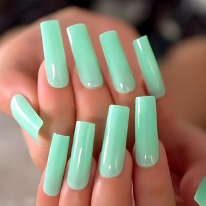 May include: A set of mint green, square-shaped artificial nails. The nails are long and have a glossy finish. The image shows a close-up of a hand with the nails applied, showcasing the color and shape of the nail enhancements.