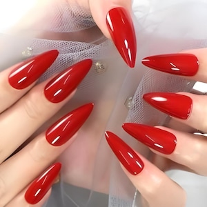May include: Close-up of a set of long, glossy, red stiletto-shaped artificial nails. The nails are evenly shaped and have a high-shine finish, reflecting light. The image showcases a manicure, highlighting the vibrant color and sleek design.