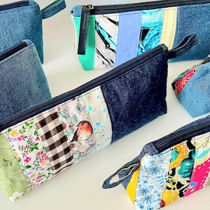 Może przedstawiać: Kolekcja dżinsowych i patchworkowych saszetek na zamek błyskawiczny. Saszetki mają różnorodne kolorowe tkaniny we wzory, w tym kwiatowe, w kratkę i ptasie. Każda saszetka ma ciemnoniebieski zamek błyskawiczny i małą pętelkę z tkaniny.