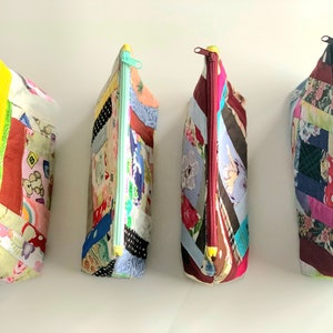 Puede incluir: Cuatro estuches con cremallera de patchwork hechos a mano. Cada estuche presenta un diseño de patchwork único con varias telas y colores. Las cremalleras son de diferentes colores, incluyendo amarillo, verde menta y burdeos. Los estuches están de pie.