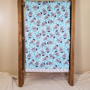 May include: A blue baby blanket with a pattern of monkeys wearing red hats. The blanket has a gray and white chevron border.
