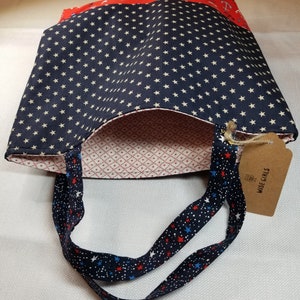 May include: A blue and white tote bag with red, white and blue stars on the straps. The bag has a red and white anchor print on the top and a blue and white star print on the bottom. The bag has a tag that says "Wise Girls".