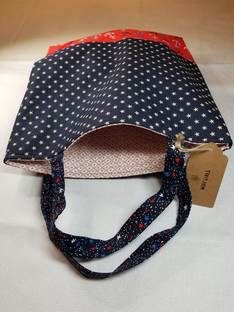 May include: A blue and white tote bag with red, white and blue stars on the straps. The bag has a red and white anchor print on the top and a blue and white star print on the bottom. The bag has a tag that says "Wise Girls".