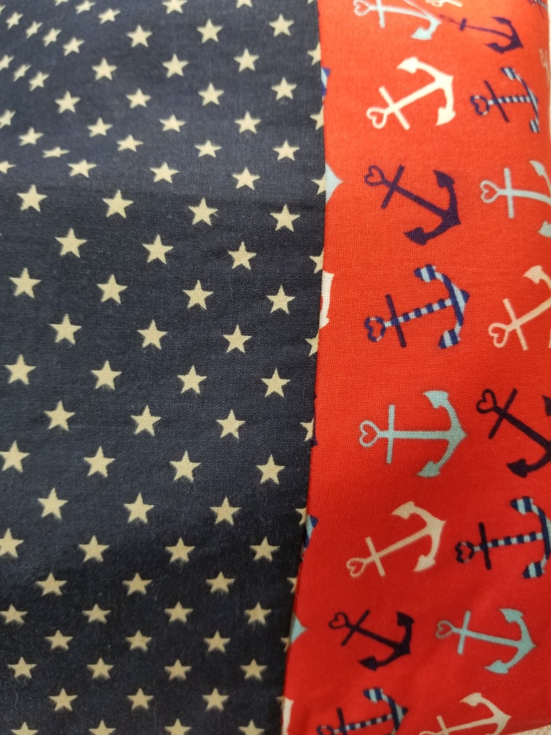 May include: A red fabric with a white and blue anchor pattern. The fabric is sewn to a navy blue fabric with a white star pattern.