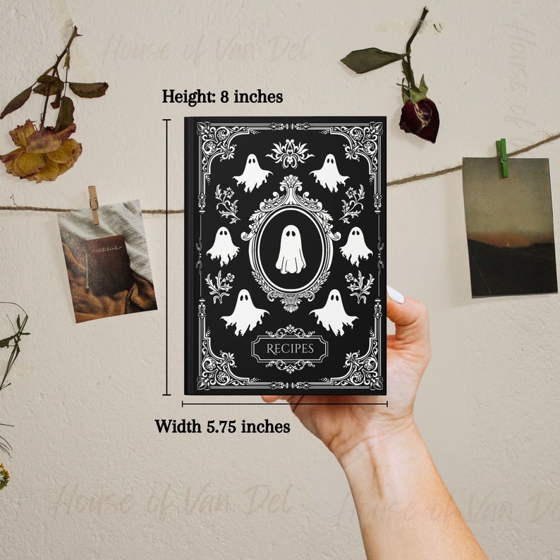 May include: Black and white recipe journal with a spooky ghost design. The cover features a black background with white ornate details and a circle with the word "RECIPES" inside. The journal measures 8 inches tall and 5.75 inches wide.