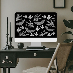 May include: A computer monitor displays a black background with a white pattern of bats, butterflies, and sprigs of lavender. The monitor sits on a black desk with a drawer and decorative knobs. Two black candles stand in ornate holders.