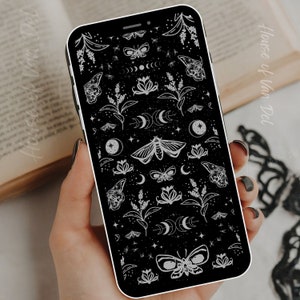 May include: A black phone case with a white pattern of moths, flowers, and crescent moons. The pattern is repeated throughout the case.
