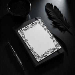 May include: A black notebook with a decorative white page featuring a black ornate border with skulls and bats. A black pen and a black feather are next to the notebook. A black bowl is in the background.
