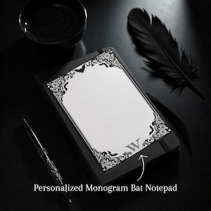 May include: A black notepad with a white page, ornate border, and a monogram letter "W". The notepad is next to a decorative pen, a black feather, and a small black bowl. The notepad is labeled "Personalized Monogram Bat Notepad".