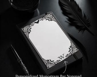 May include: A black notepad with a white page, ornate border, and a monogram letter "W". The notepad is next to a decorative pen, a black feather, and a small black bowl. The notepad is labeled "Personalized Monogram Bat Notepad".
