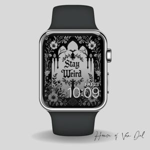 Pode incluir: Um smartwatch preto com moldura prateada e pulseira preta. O mostrador mostra as palavras "Stay Weird" em uma fonte gótica, rodeadas por elementos florais e góticos. A hora é 10:09.