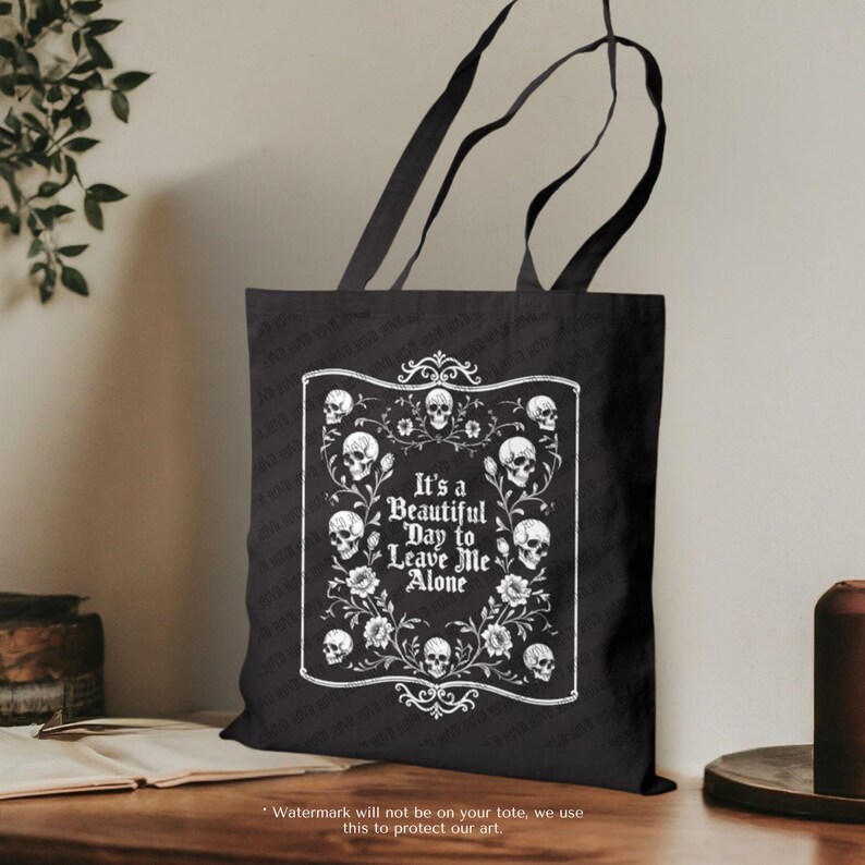 May include: Black tote bag with a white graphic design. The design features skulls, flowers, and the text "It's a Beautiful Day to Leave Me Alone" in a decorative frame. The bag has black handles.
