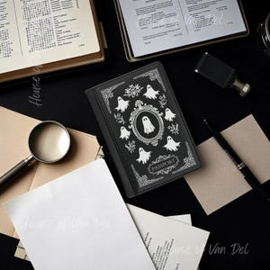 May include: Black passport holder with a white ghost design and the word "PASSPORT" printed on the front.