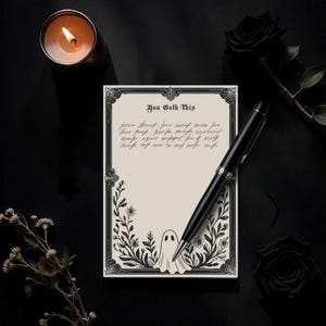 May include: A notepad with the text "You Goth This" in a decorative frame, featuring a ghost illustration and floral accents. A black pen rests on the notepad, with a lit candle and black rose in the background. The overall theme is gothic.