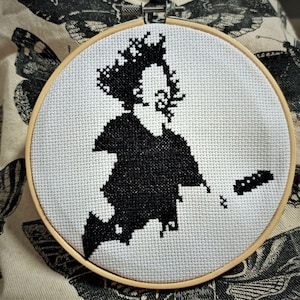 May include: Black and white cross-stitch embroidery of a person's silhouette in a hoop.