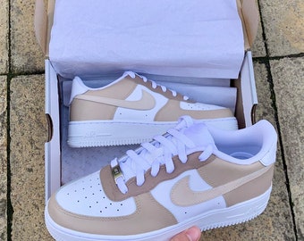 May include: A pair of white and beige sneakers with a white swoosh logo. The sneakers are in a white box with tissue paper.