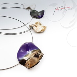 May include: A silver chain necklace with four ceramic pendants. The pendants are shaped like petals and are painted in shades of white, gray, brown, and purple.