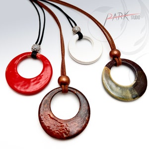 May include: Three ceramic circle pendants on leather cords. The pendants are red, white, and brown with a speckled glaze.
