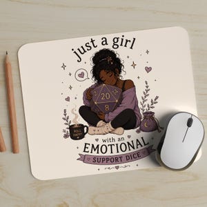 May include: A rectangular mouse pad featuring an illustration of a person hugging a large purple twenty-sided die. The text reads "just a girl with an EMOTIONAL SUPPORT DICE" and "ROLL HAPPY" on a mug. The design includes hearts, stars, and plants.