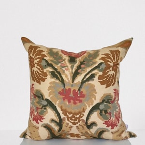 Puede incluir: Una almohada decorativa con un patrón floral en tonos marrones, rojos y verdes. La almohada tiene un fondo de color crema y presenta un gran diseño floral con detalles intrincados.