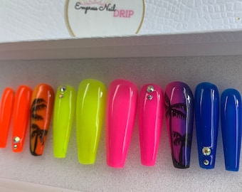 May include: Set of ten long, colourful, false nails with a palm tree design. The nails are in shades of orange, yellow, pink, and blue. Each nail has a clear rhinestone on top.
