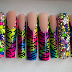 May include: Set of ten long, almond-shaped false nails with a colorful zebra print design. The nails are decorated with rhinestones, glitter, and small charms.