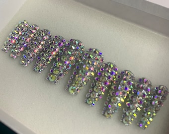May include: A set of iridescent rhinestones arranged in a cascading pattern. The rhinestones are small and have a variety of colors, including purple, blue, and green.