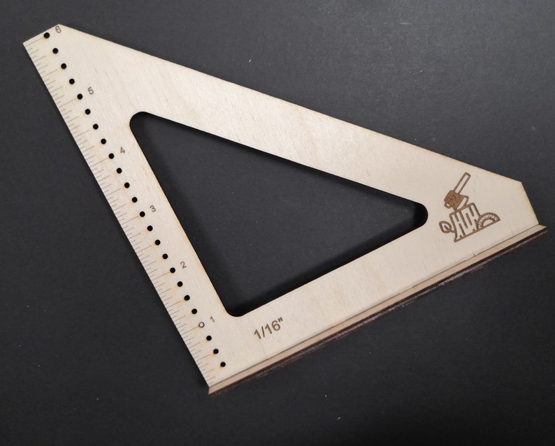 May include: A wooden triangle ruler with a 1/16 inch scale and a small axe and log design. The ruler has a 6-inch scale on one side.
