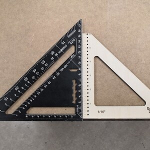 May include: A black and white combination square with markings in inches. The black square has a ruler on two sides and a protractor on the third side. The white square has a ruler on one side and a protractor on the other side. The white square has a small logo of an axe on a tree stump.