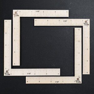 May include: Four wooden rulers with markings in inches and 1/16ths of an inch. The rulers are arranged in a square shape.