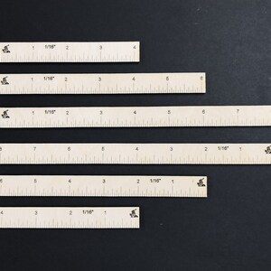 May include: Six white rulers of different lengths, each marked with 1/16 inch increments. The rulers are arranged vertically on a black background.