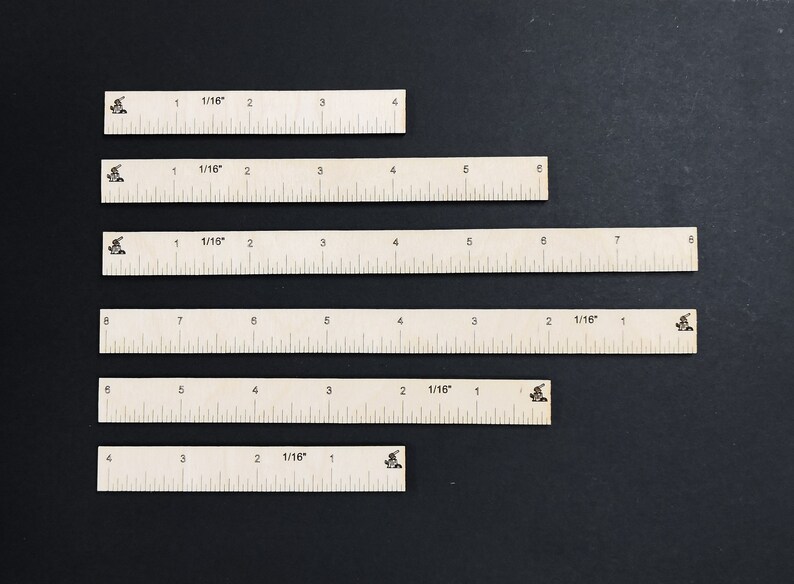 May include: Six white rulers of different lengths, each marked with 1/16 inch increments. The rulers are arranged vertically on a black background.