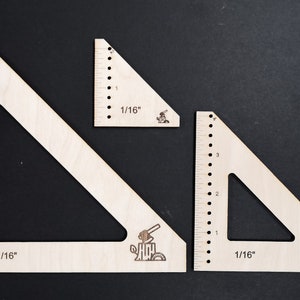 May include: Three wooden triangles with markings in 1/16 inches. The triangles are different sizes and have a small illustration of a saw and a tree stump on each.