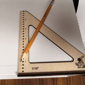May include: A wooden triangle ruler with a pencil on top of it. The ruler has a 1/16 inch marking and a small wood carving of an axe on a stump.