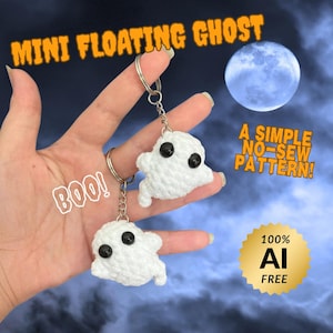 May include: Two white crocheted ghost keychains with black plastic eyes attached to silver metal key rings. The image includes text reading MINI FLOATING GHOST, A SIMPLE NO-SEW PATTERN!, BOO!, and a gold seal stating 100% AI FREE.