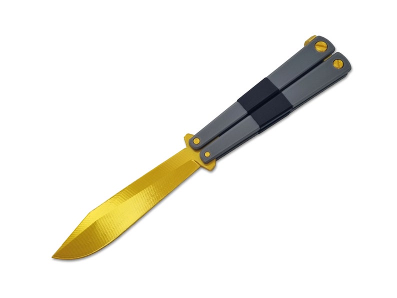 May include: A butterfly knife with a gold-colored blade and accents. The handle is gray with a black center section and gold-colored screws. The knife is open, displaying the full blade.