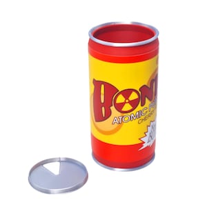 Może przedstawiać: Cylindryczna puszka w kolorze czerwono-ż&oacute;łtym z napisem "DONK" w kolorze czerwonym i symbolem promieniowania w literze "O". Na puszce napis "Atomic Punch Cherry". Obok puszki leży srebrna pokrywka. Puszka ma około 12 cm wysokości.