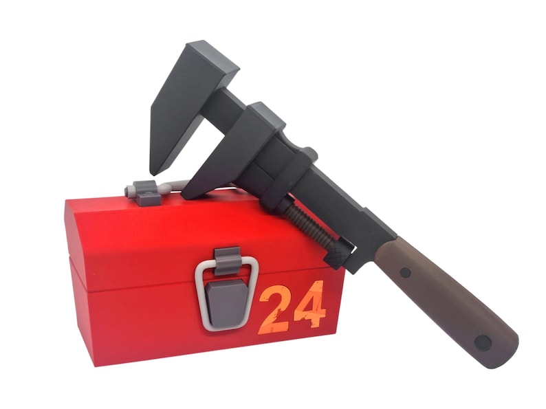May include: A red toolbox with a gray handle and the number "24" in orange. A black adjustable wrench with a brown handle rests on top of the toolbox. The wrench is angled across the toolbox.