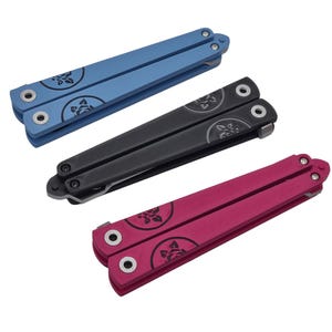 Op de afbeelding: Drie vlindermessen in blauw, zwart en magenta. Elk mes heeft een bloemenpatroon op de handvatten. De messen worden op een witte achtergrond gepresenteerd.