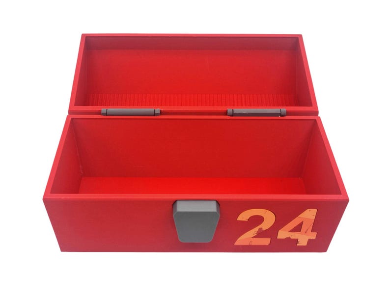 May include: A red wooden toolbox with an open lid. The box has a gray latch and the number "24" in orange on the front. The interior of the box is also red.