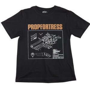 May include: A black short-sleeve t-shirt featuring the text PROP FORTRESS in tan letters above a white technical blueprint graphic of a scattergun weapon. The design includes detailed exploded-view components and technical labels in a box.
