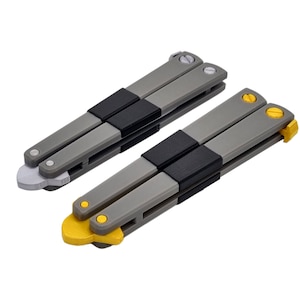 May include: Two butterfly knives with gray handles, black center grips, and silver or yellow accents. The blades are folded, showcasing the design and color variations. The knives are set against a white background.