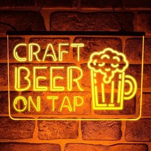 Op de afbeelding: Neon-bord met gele tekst die "CRAFT BEER ON TAP" luidt en een gele omtrek van een bierglas met schuim erop.