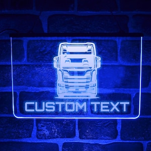 May include: A blue neon sign featuring a truck design with the words "CUSTOM TEXT" in white. The sign is rectangular with a glowing outline and is mounted on a brick wall.