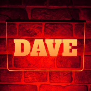 Peut inclure: Enseigne au néon avec le nom "DAVE" en grandes lettres blanches et grasses. L'enseigne dégage une lueur orange chaude et est placée sur un mur de briques rouges. L'enseigne est rectangulaire et bordée de noir.