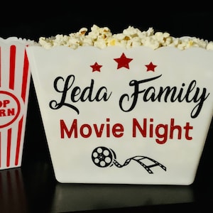May include: White popcorn containers with red and white stripes. One container has the text "Leda Family Movie Night" with a film reel graphic. Other containers have names: Brian, Anetta, Jonathan, and "Pop Corn".