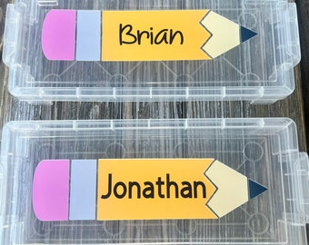 May include: Two clear plastic storage boxes with yellow pencil-shaped labels. The top box has the name "Brian" on the label. The bottom box has the name "Jonathan" on the label.