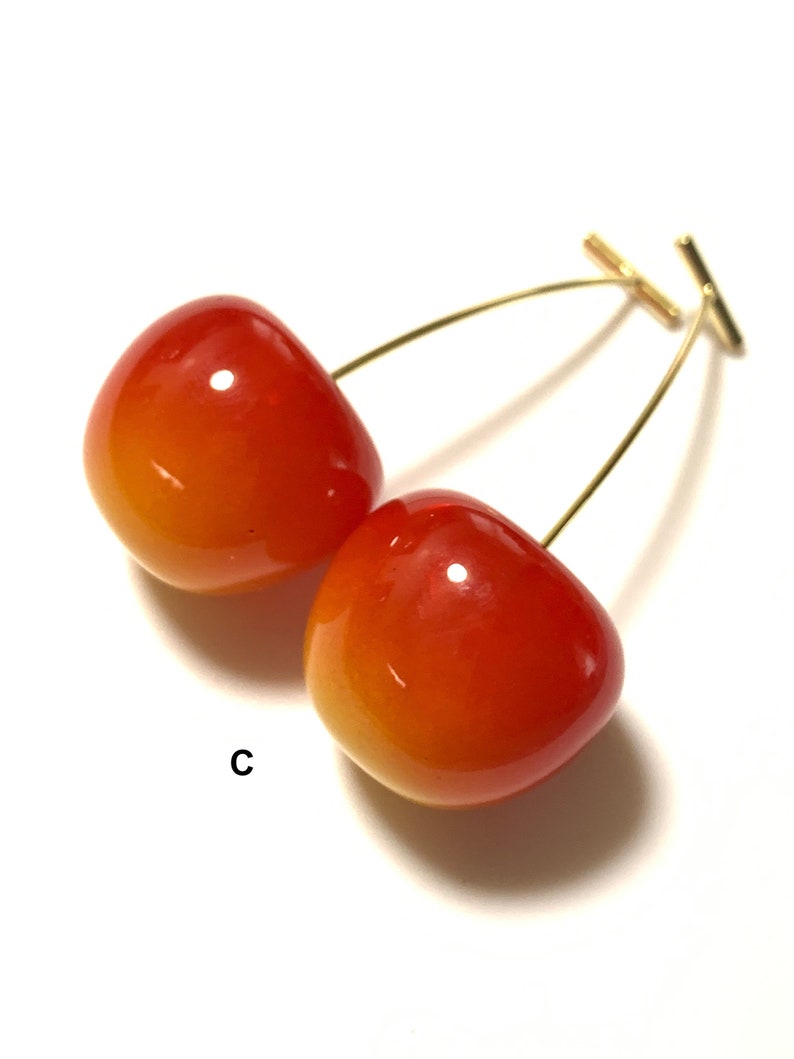 K&ouml;nnte beinhalten: Ein Paar Kirsch-Ohrringe mit goldfarbenem Draht und einem T-f&ouml;rmigen Verschluss. Die Kirschen sind rot und orange mit einem Farbverlauf.